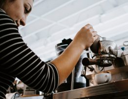 Image of a woman holding down a espresso machine, pouring coffee into the cup.